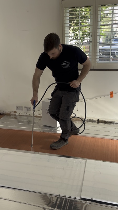 Jake using a laser level on an in-progress UFH install